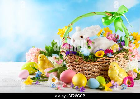 Easter composition with little white bunny in basket, chicks, spring flowers and colorful Easter eggs . Easter Card with copy space. - Photomontage Stock Photo