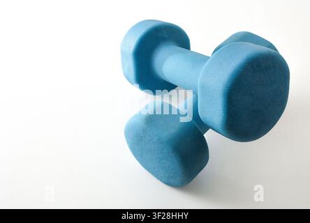 Two blue neoprene dumbbells resting on a clean white surface with soft natural light and subtle shadows. Minimal fitness concept with copy space and a Stock Photo