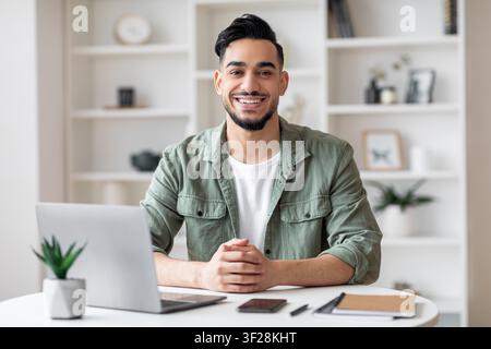 Smiling Young Hispanic Man Working At Laptop In Home Office, Business Concept Stock Photo