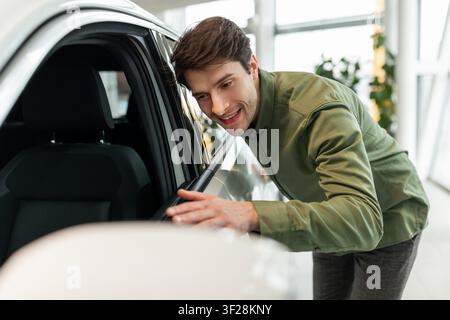 Young Man Smiling And Inspecting Car In Showroom, Business Concept Stock Photo