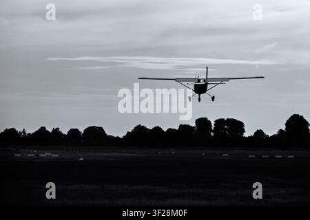Small Cessna light aircraft on final approach to land at a grass airfield at dusk, Netherlands Stock Photo