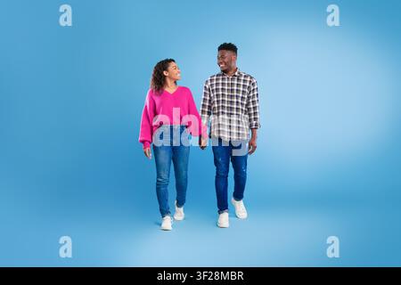 Happy Young Couple Holding Hands And Smiling Walking On Blue Background Stock Photo