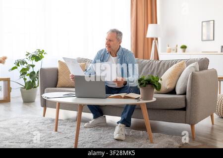 Elderly Caucasian Man Analyzing Business Reports At Home, Focused Expression, Home Office Concept Stock Photo