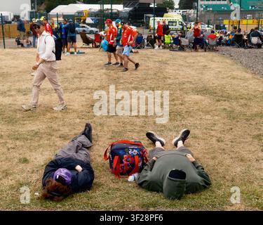 Fans waiting between events at Silverstone during the British Grand Prix weekend, resting on the grass while other spectators move through the circuit Stock Photo