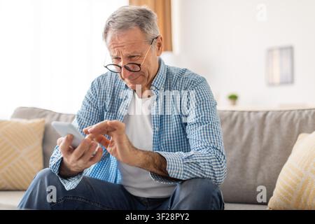 Elderly Caucasian Man Using Smartphone With Glasses, Home Setting, Focused Emotion Stock Photo