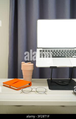 Clean workspace featuring laptop on stand, glasses, notebook, and coffee cup, minimalist home office concept. Stock Photo