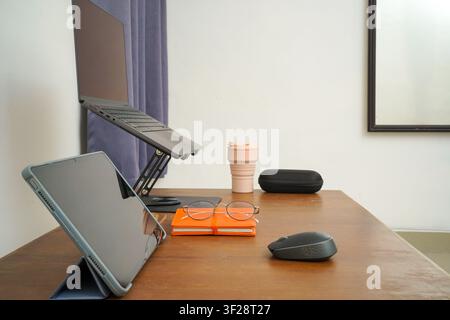 Side view of modern workspace with laptop stand, tablet, mouse, and accessories on wooden desk for productivity. Stock Photo