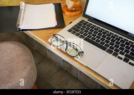 Reading glasses placed on laptop beside notebook and coffee on wooden desk, creating a cozy and productive study workspace at home. Stock Photo