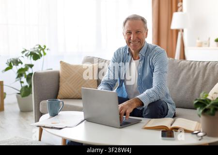Happy Elderly Caucasian Man Working On Laptop At Home, Relaxed Lifestyle Stock Photo