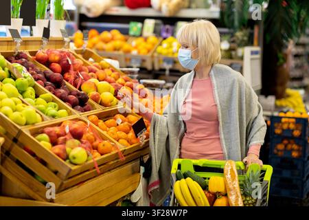 Senior Woman Wearing Face Mask Shopping For Fresh Fruits In Supermarket, Healthy Eating Concept Stock Photo