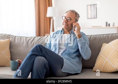 Smiling Elderly Caucasian Man Talking On Phone While Relaxing On Couch At Home, Lifestyle Concept Stock Photo