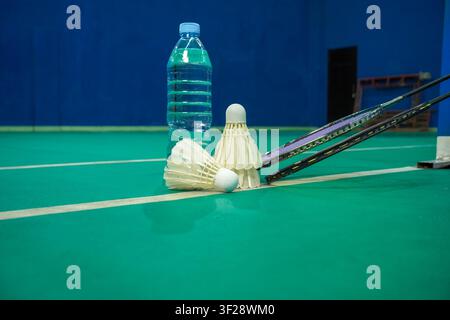Badminton rackets, shuttlecocks, and a water bottle arranged on an indoor badminton court. Sports equipment and fitness training concept with copy spa Stock Photo