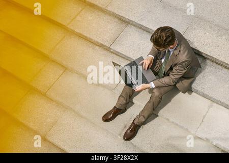 Adult Businessman Working on Laptop on Steps in Urban Setting Stock Photo