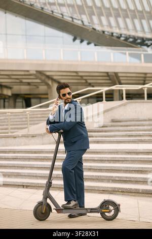 Indian Adult Businessman Talking on Phone on Electric Scooter Stock Photo
