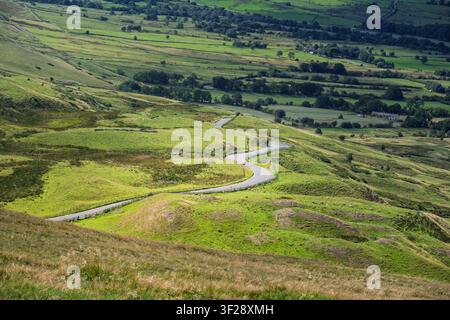 An elevated view of a winding asphalt country road curving through the rolling green hills near Mam Tor, leading down toward Edale, Derbyshire, UK Stock Photo