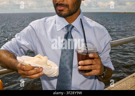 Indian Businessman Eating Lunch and Drinking Iced Coffee Outdoors Stock Photo