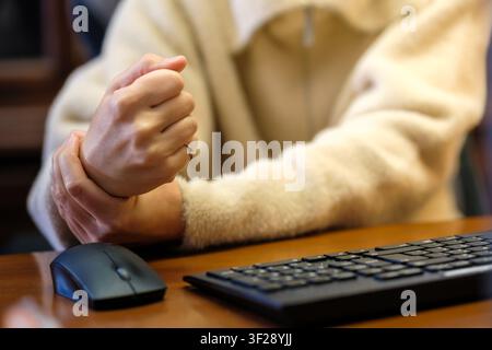 Woman holding her sore wrist feeling pain while working with a computer mouse and keyboard Stock Photo