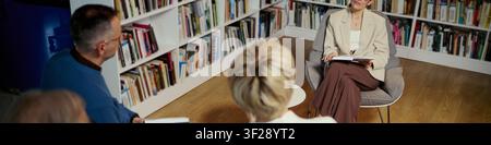 Header of middle aged adults sitting and discussing in counseling session, sharing thoughts in library setting. Suitable for mental health therapy, coaching, support group marketing, wide shot Stock Photo
