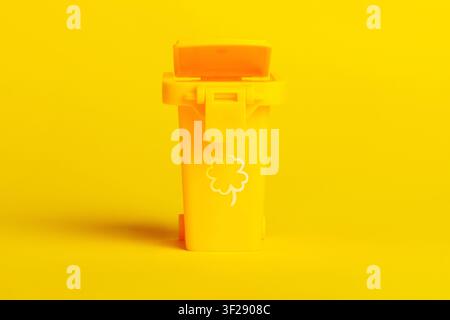 Minimalist yellow trash bin with clover icon, isolated on vibrant yellow background. Modern waste management and eco-friendly concept. Stock Photo