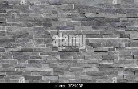 Stone coating wall made of striped stacked bricks of natural gray and brown rocks. External wall covering, background and texture. Stock Photo