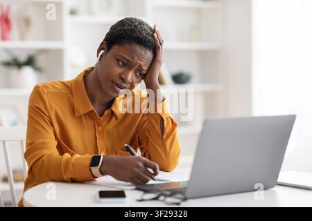 Worried Black Woman Working On Laptop Taking Notes In Modern Office, Business Concept Stock Photo