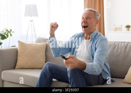 Happy Elderly Caucasian Man Celebrating While Watching Tv At Home, Excited Emotion Stock Photo