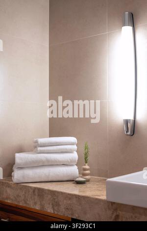 Rolled white towel on a wooden bath tray with spa essentials in a modern hotel bathroom, creating a relaxing wellness atmosphere Stock Photo