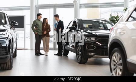 Couple Talking With Salesman In Car Showroom, Test Driving Black Suv, Business Concept Stock Photo