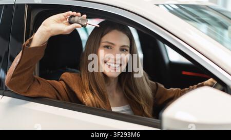Happy Young Woman Holding Car Key Inside New Vehicle, Excited About Purchase, Business Concept Stock Photo