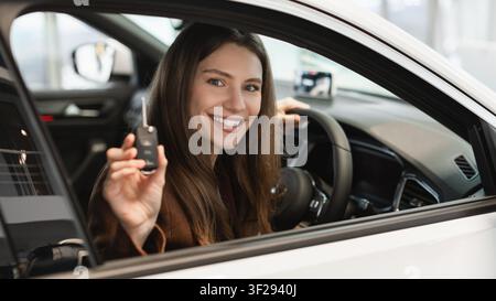 Happy Young Woman Driving New Car And Holding Key Inside Vehicle, Car Ownership Concept Stock Photo