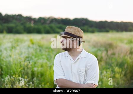 Young man in straw hat standing in summer meadow at golden hour Stock Photo