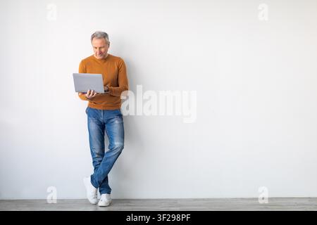 Senior Caucasian Man Using Laptop While Leaning Against Wall, Business Concept Stock Photo