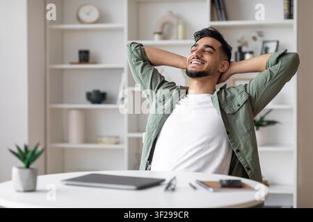 Smiling Young Asian Man Relaxing In Office With Hands Behind Head, Business Concept Stock Photo
