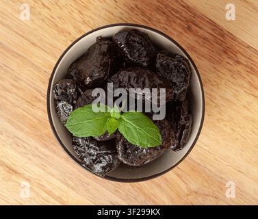 Dry Plums, Dried Black Fruits in Bowl, Prune Group, Natural Dessert, Healthy Diet, Dry Plum Fruit on Wooden Table Background Stock Photo