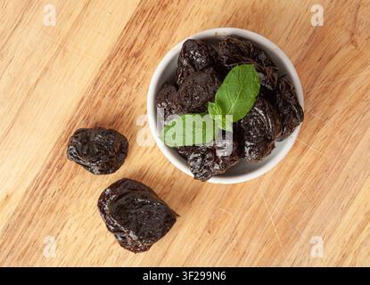 Dry Plums, Dried Black Fruits in Bowl, Prune Group, Natural Dessert, Healthy Diet, Dry Plum Fruit on Wooden Table Background Stock Photo