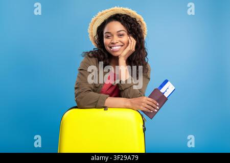 Smiling Young Black Woman With Passport And Yellow Suitcase Preparing For Travel Stock Photo