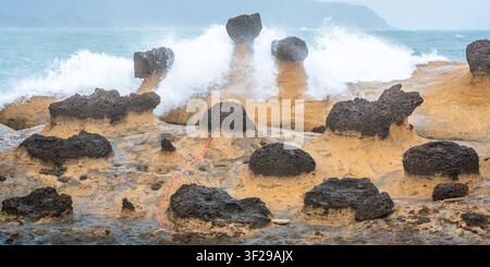 Scenic view of hoodoo stones rock formation with wave crashing on rocks in Yehliu geopark in New Taipei Taiwan Stock Photo