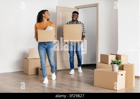 Happy Young Black Couple Carrying Cardboard Boxes While Moving Into New Home, Moving Concept Stock Photo