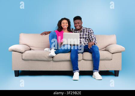 Happy Black Couple Using Laptop Together On Couch At Home, Family Concept Stock Photo