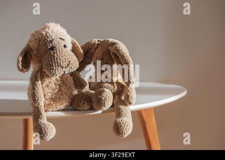 Plush sheep and bunny stuffed animals sit on a simple white table, with warm sunlight illuminating their soft, crocheted textures, evoking innocence a Stock Photo