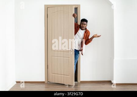 Confused Black Man Peeking Through Open Door, Surprised At Unexpected Situation, Home Setting Stock Photo