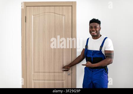 Happy Black Male Repairman Pointing At Closed Door In Interior Setting Stock Photo