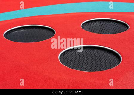 Three round in-ground trampolines with black woven mesh on red rubber playground flooring Stock Photo