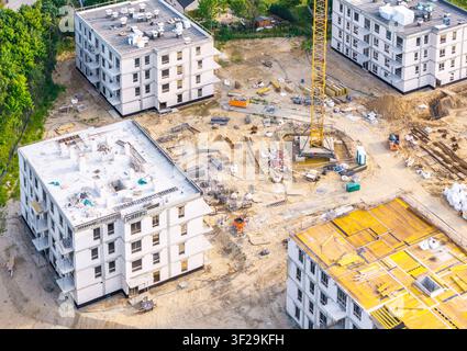 Aerial view of a residential construction site featuring several multi-story buildings, a yellow tower crane, and raw earth ground in Kowale, Pomerani Stock Photo