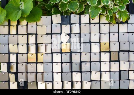 Square metal sequins on a matrix panel combined with green plants at the top. Shimmering silver and gold metallic texture with natural variegated leav Stock Photo