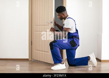 Man Repairing Door Lock In Blue Overalls, Focused Attention On Task, Home Setting Stock Photo