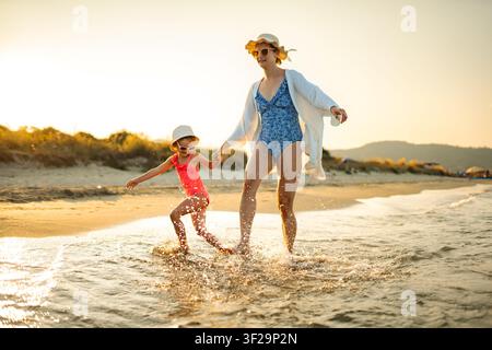 Mother and daughter splashing water on summer beach vacation at sunset Stock Photo
