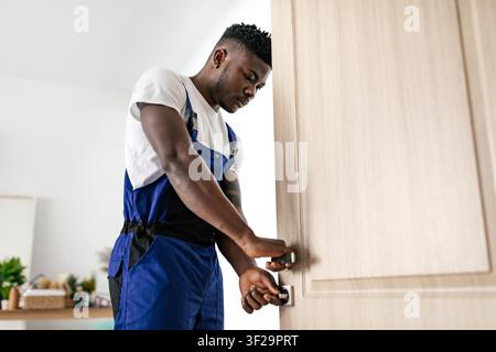 Young Black Man Fixing Door Lock With Focused Expression, Home Interior Setting Stock Photo