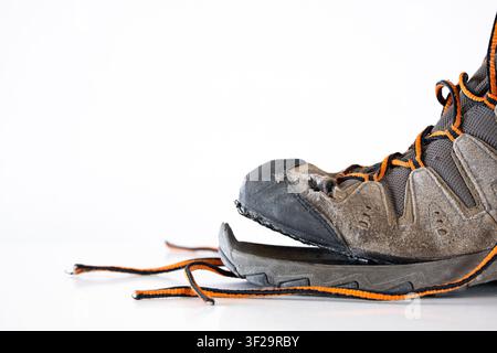 A detailed side view close up studio shot of an old, heavily worn out trekking shoe showing a broken, completely detached gray rubber sole at the toe Stock Photo