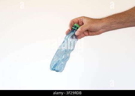 A minimalist studio shot of a person hand holding a squeezed, wrinkled blue plastic beverage bottle with a green cap down at an angle against a clean, Stock Photo
